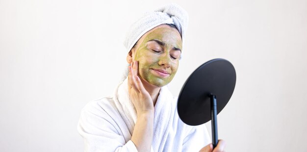 Jeune femme avec un masque vert sur son visage dans un peignoir devant un miroir