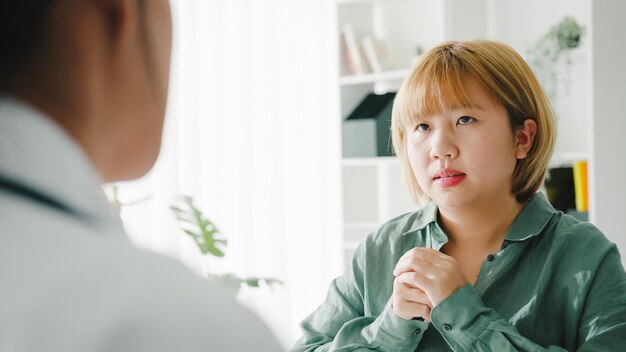 Jeune femme médecin asiatique en uniforme médical blanc discutant des résultats ou des symptômes avec une patiente