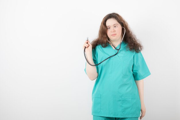 Jeune femme médecin atteinte du syndrome de Down à l'aide d'un stéthoscope sur un mur blanc.