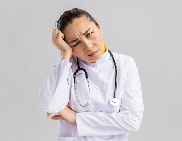 Jeune femme médecin en blouse blanche avec stéthoscope autour du cou agacé et irrité