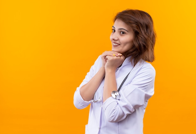 Jeune femme médecin en blouse blanche avec stéthoscope à la sortie et heureux tenant les bras ensemble en attente de surprise