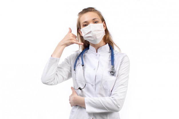 Jeune femme médecin en combinaison médicale blanche en stéthoscope masque de protection blanc posant sur le blanc