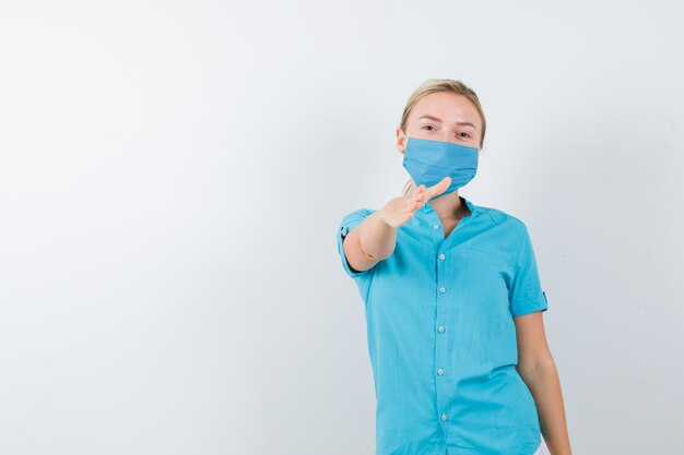 Jeune femme médecin étirant la main pour saluer en uniforme et avoir l'air confiant