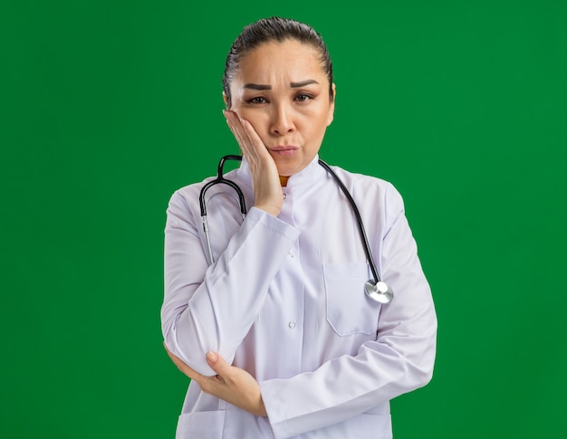 Jeune femme médecin fatiguée et ennuyée avec la main sur sa joue