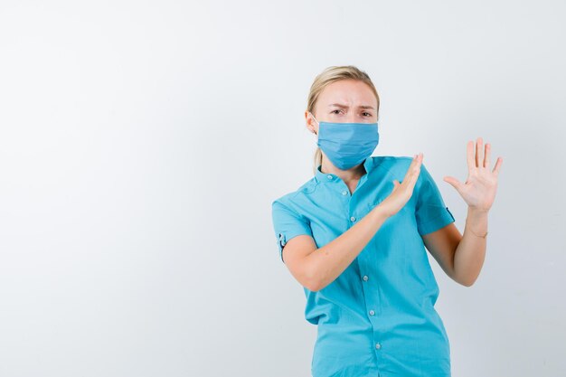 Jeune femme médecin gardant la main pour se défendre en uniforme et ayant l'air effrayée isolée