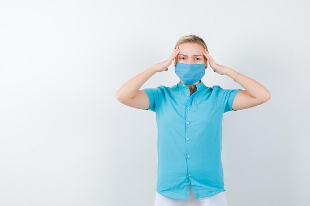 Jeune femme médecin gardant les mains sur les temples en uniforme médical