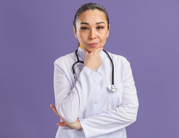 Jeune femme médecin avec la main sur le menton avec une expression confiante