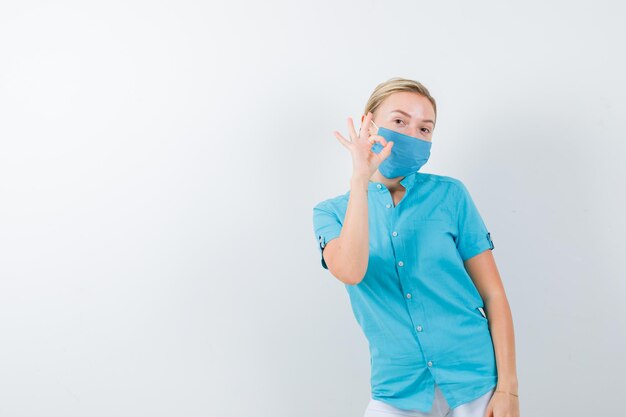 Jeune femme médecin montrant un geste correct en uniforme médical, masque et à la gaieté