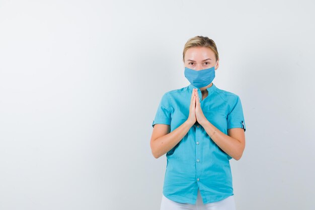 Jeune femme médecin montrant les mains jointes dans un geste de plaidoirie en uniforme médical