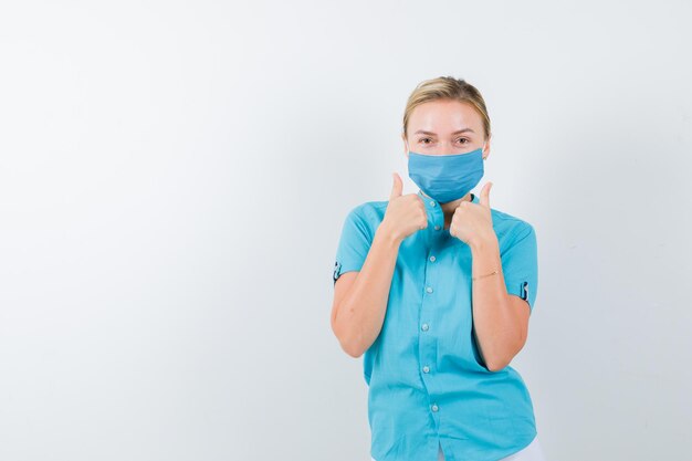 Jeune femme médecin montrant les pouces vers le haut en uniforme et à la confiance isolée