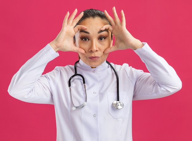 Jeune femme médecin ouvrant grand les yeux avec les doigts