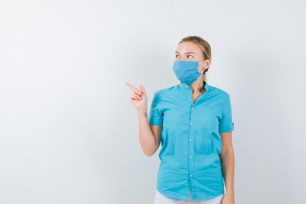 Jeune femme médecin pointant vers le coin supérieur gauche en uniforme médical