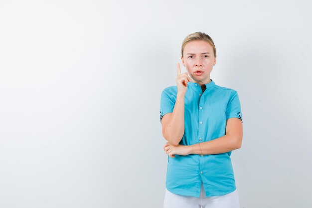 Jeune femme médecin pointant vers le haut en uniforme médical, masque et semblant perplexe