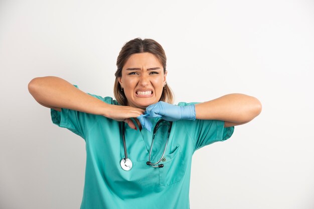 Jeune femme médecin portant des gants en latex et des gommages sur fond blanc.