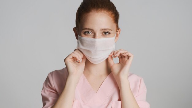 Jeune femme médecin portant un masque médical à la caméra sur fond blanc Concept de sécurité