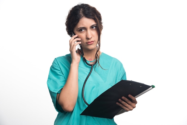 Jeune femme médecin avec presse-papiers et parler au téléphone portable sur fond blanc