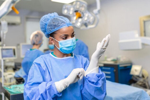 Une jeune femme médecin se prépare à la chirurgie porte des gants chirurgicaux bleus dans un manteau et un masque