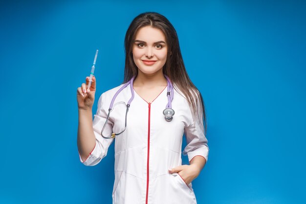 Jeune femme, médecin avec une seringue à la main. Portrait moyen plan. Une seringue dans la main d'une femme sur bleu.