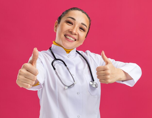 Jeune femme médecin souriant avec un visage heureux montrant les pouces vers le haut