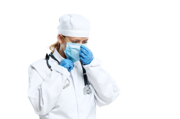 Jeune femme médecin avec stéthoscope et masque facial isolé sur mur blanc