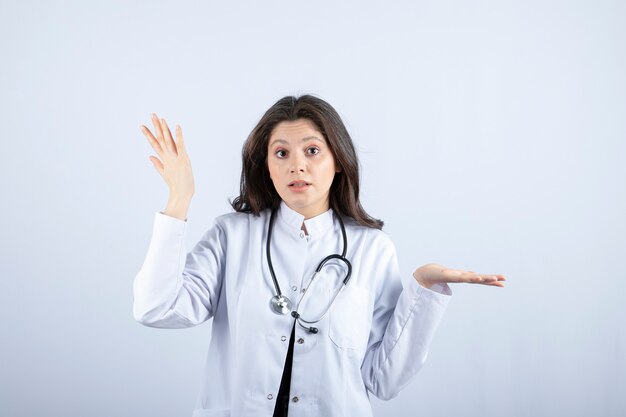 Jeune femme médecin avec stéthoscope posant à la caméra sur un mur blanc.