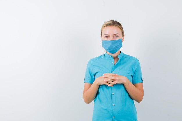 Jeune femme médecin tenant les mains jointes sur la poitrine en uniforme isolé