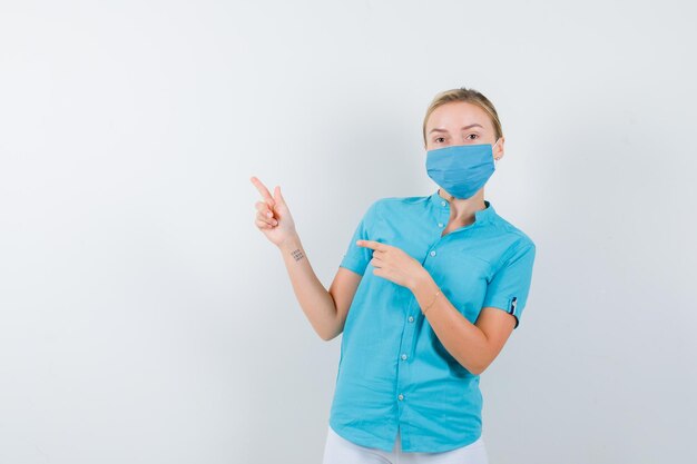 Jeune femme médecin en uniforme médical, masque pointant vers le coin supérieur gauche