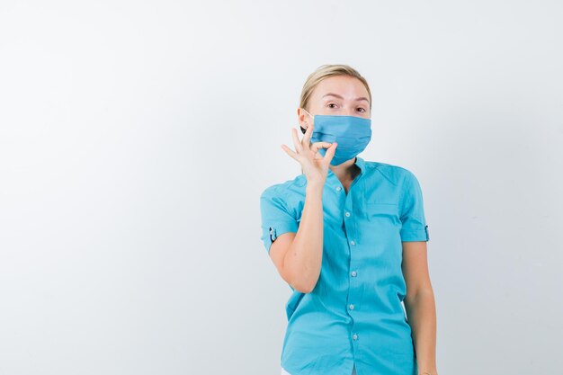 Jeune femme médecin en uniforme montrant un geste ok et ayant l'air confiant isolé