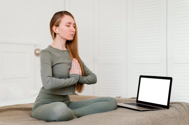 Jeune femme méditant à la maison avec un ordinateur portable à côté