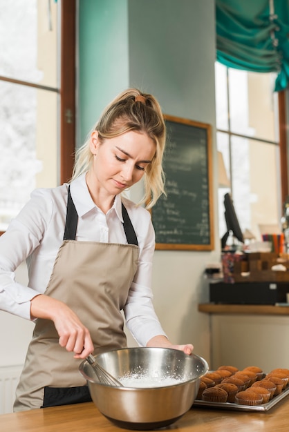 Jeune femme mélangeant la pâte au fouet dans l&#39;ustensile préparant le cupcake