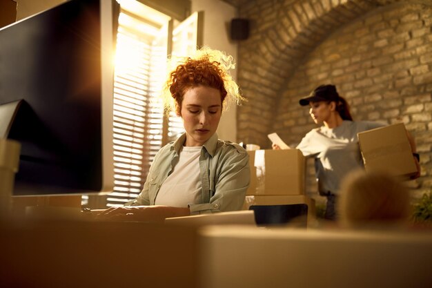 Jeune femme mettant à jour les détails de la commande tout en préparant les colis pour une livraison au bureau