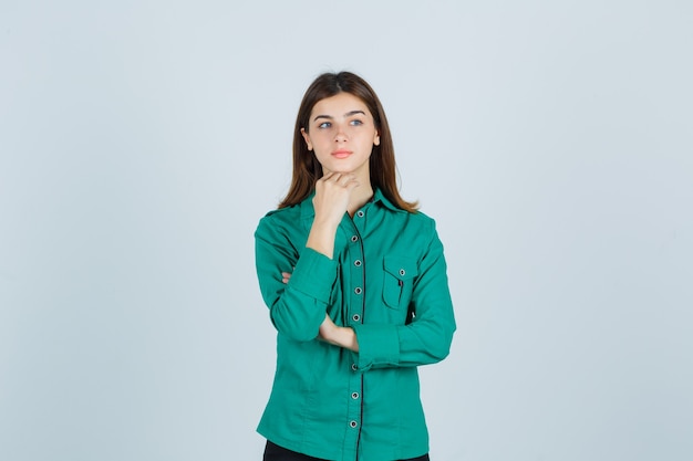 Jeune femme mettant la main pour appuyer sur le menton en chemise verte et regardant pensif, vue de face.