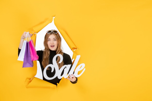 Jeune femme de mode avec des sacs à provisions à travers un trou de papier déchiré dans le mur