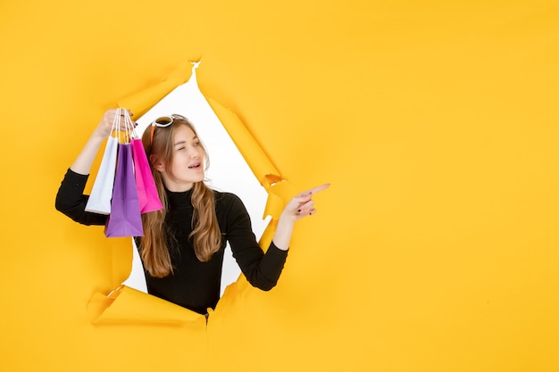 Jeune femme de mode avec des sacs à provisions à travers un trou de papier déchiré dans le mur