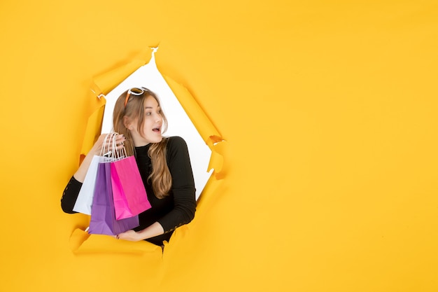 Jeune femme de mode avec des sacs à provisions à travers un trou de papier déchiré dans le mur