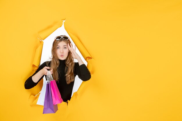 Jeune femme de mode avec des sacs à provisions à travers un trou de papier déchiré dans le mur