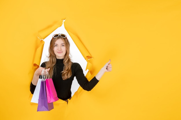 Jeune femme de mode avec des sacs à provisions à travers un trou de papier déchiré dans le mur