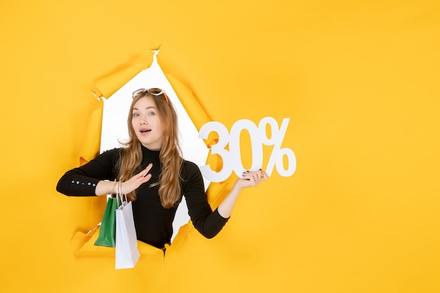 Jeune femme de mode tenant des sacs à provisions et pourcentage de remise à travers un trou de papier déchiré dans le mur