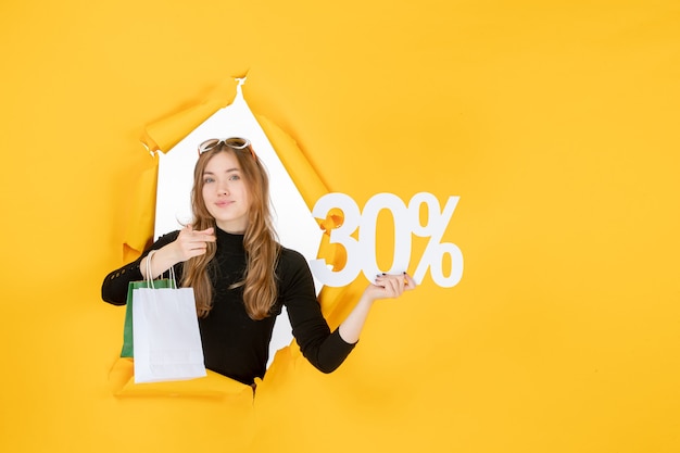 Jeune femme de mode tenant des sacs à provisions et pourcentage de remise à travers un trou de papier déchiré dans le mur