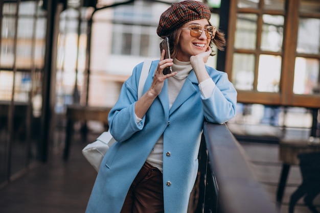 Jeune femme modèle en manteau bleu par le café, à l'aide de téléphone