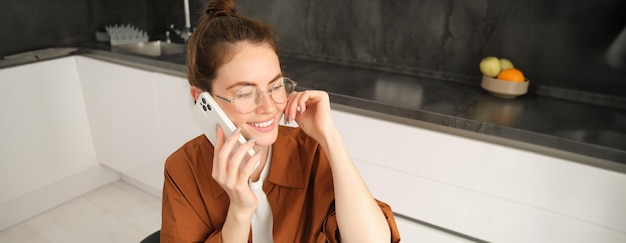 Photo gratuite une jeune femme moderne assise dans la cuisine avec un smartphone qui parle au téléphone portable a un ami