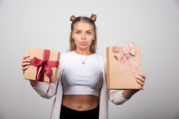 Jeune femme montrant des cadeaux de vacances sur mur gris.