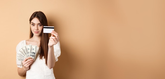 Photo gratuite une jeune femme montrant une carte de crédit en plastique préfère le paiement sans contact au lieu de billets d'un dollar debout