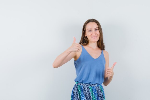 Jeune femme montrant deux pouces vers le haut en maillot, jupe et à la joyeuse, vue de face.