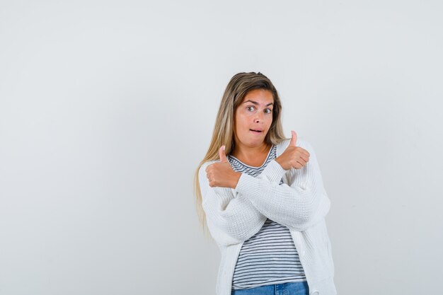 Jeune femme montrant deux pouces vers le haut en t-shirt, veste et regardant heureux, vue de face.