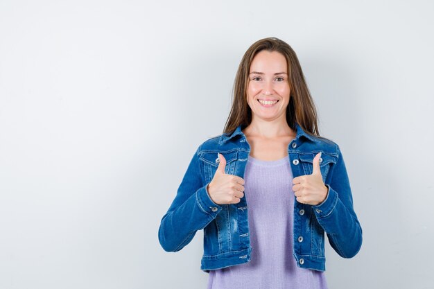 Jeune femme montrant un double coup de pouce en t-shirt, veste et l'air heureux, vue de face.