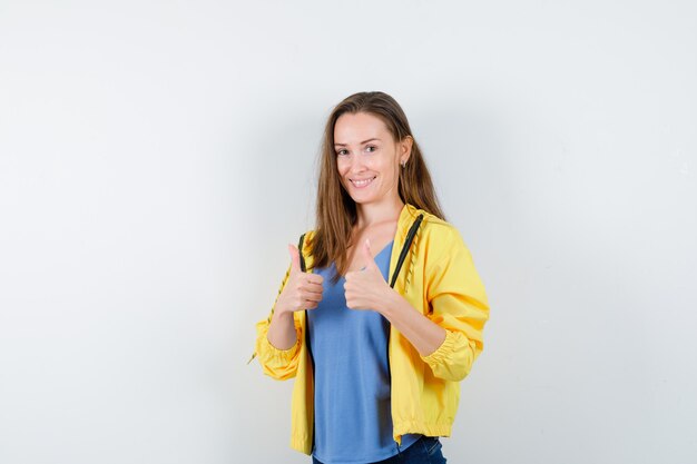 Jeune femme montrant un double pouce levé et l'air confiant, vue de face.