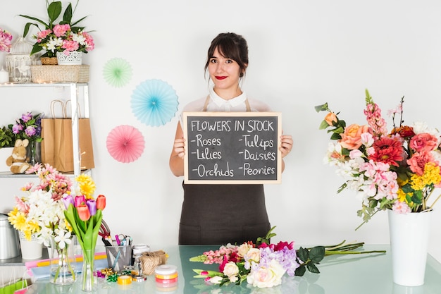 Photo gratuite jeune femme montrant des fleurs en stock sur ardoise