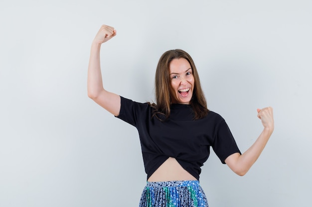 Jeune femme montrant le gagnant pose en t-shirt noir et jupe bleue et à la recherche attrayante