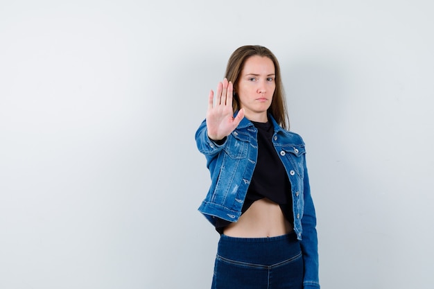 Jeune femme montrant un geste d'arrêt en blouse et semblant résolue. vue de face.